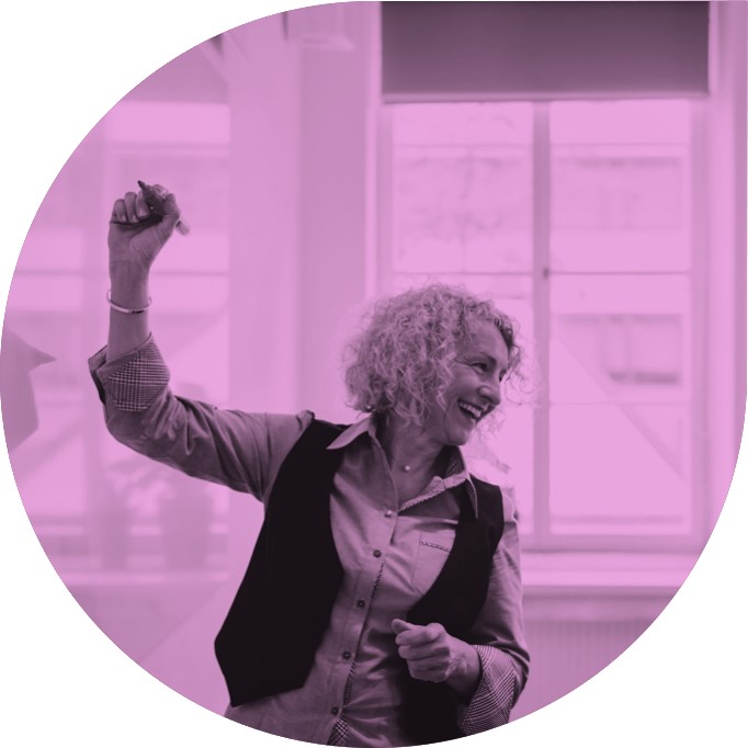 Image shows a teacher in her mid forties smiling at the class whilst writing on the white board